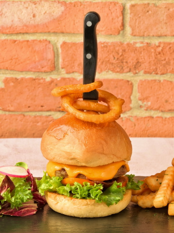 Burger with cheese stabbed by a knife served with onion rings