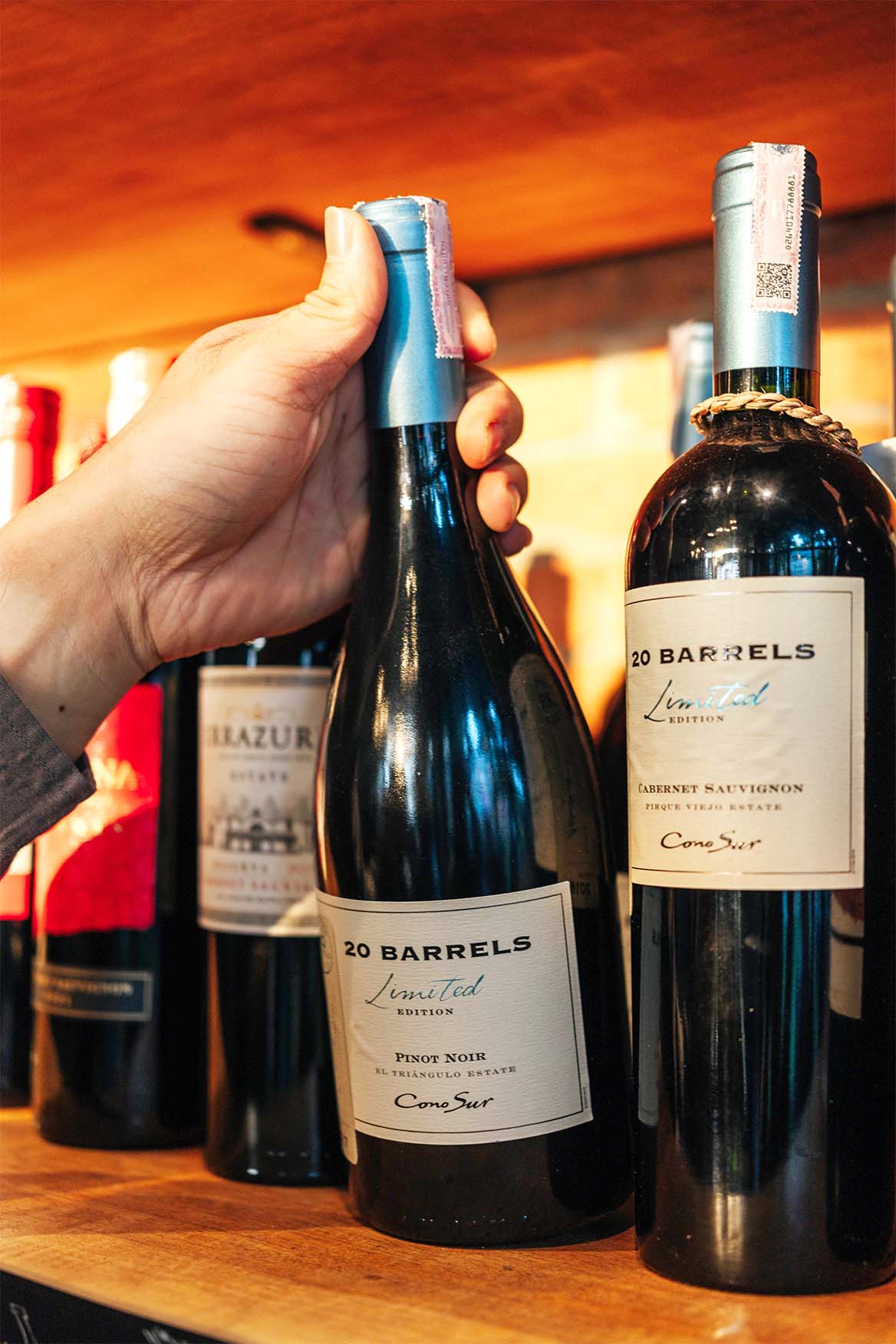 A Person Picking A Wine Bottle From The Shelf