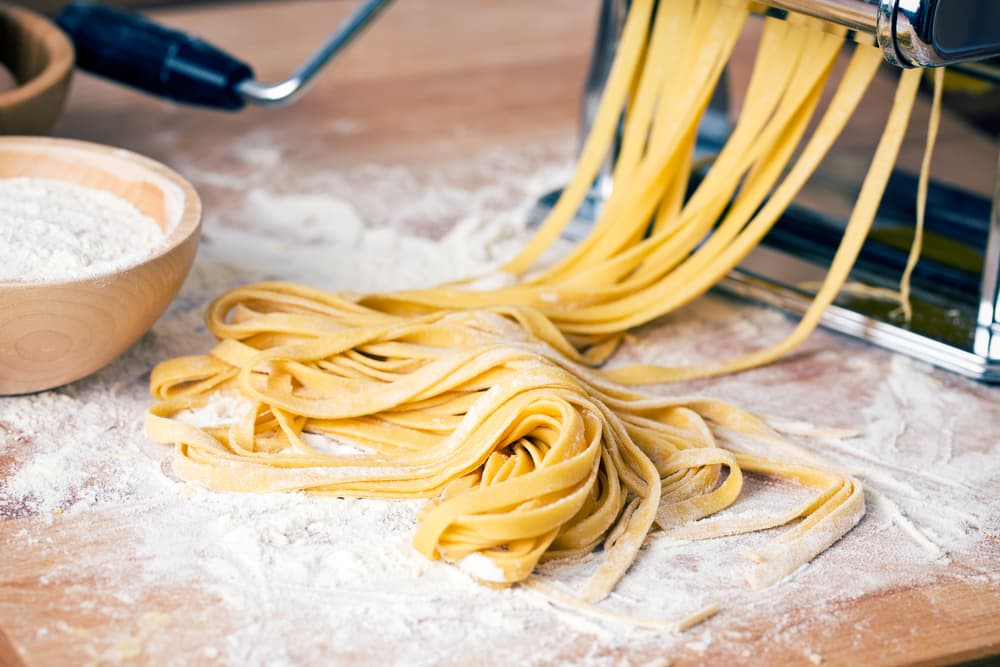 Fresh linguine pasta is cut as its pressed through a pasta maker