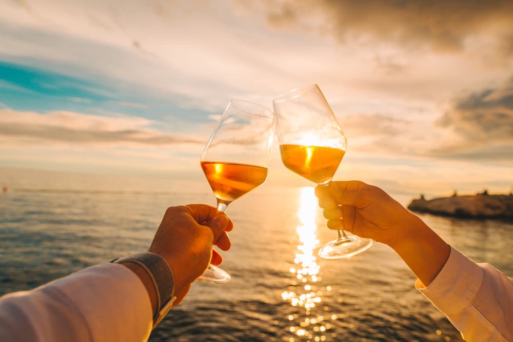 Two friends cheering while drinking wine on the beach